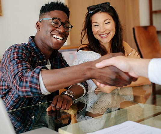 Young couple meeting with person in office shaking hands.