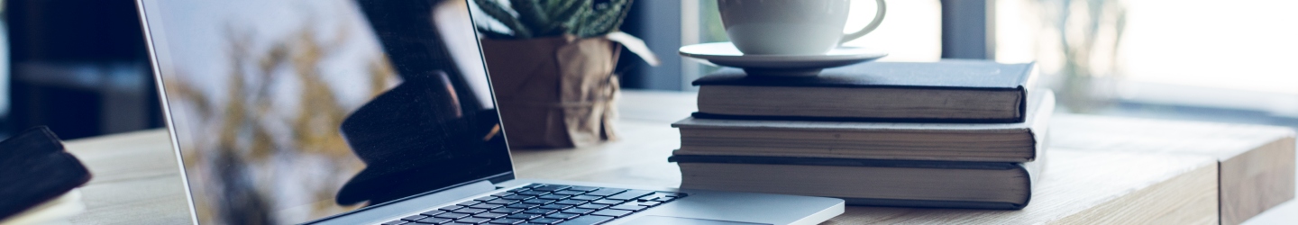 Cup of coffee sitting atop a small stack of books next to an open laptop.